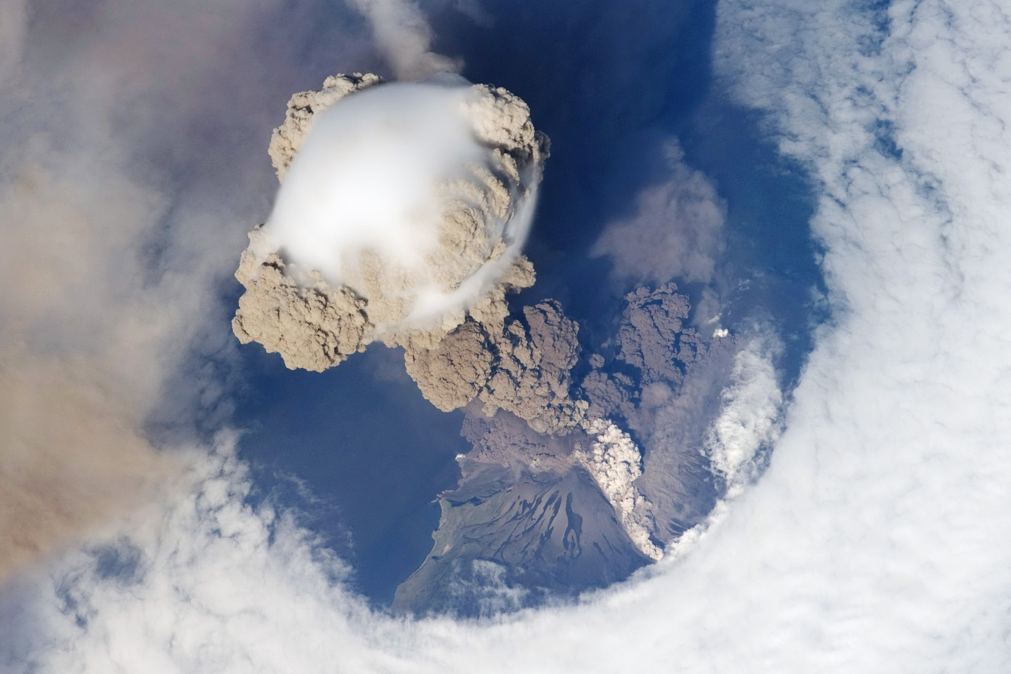 An eruption column rises above an island volcano.