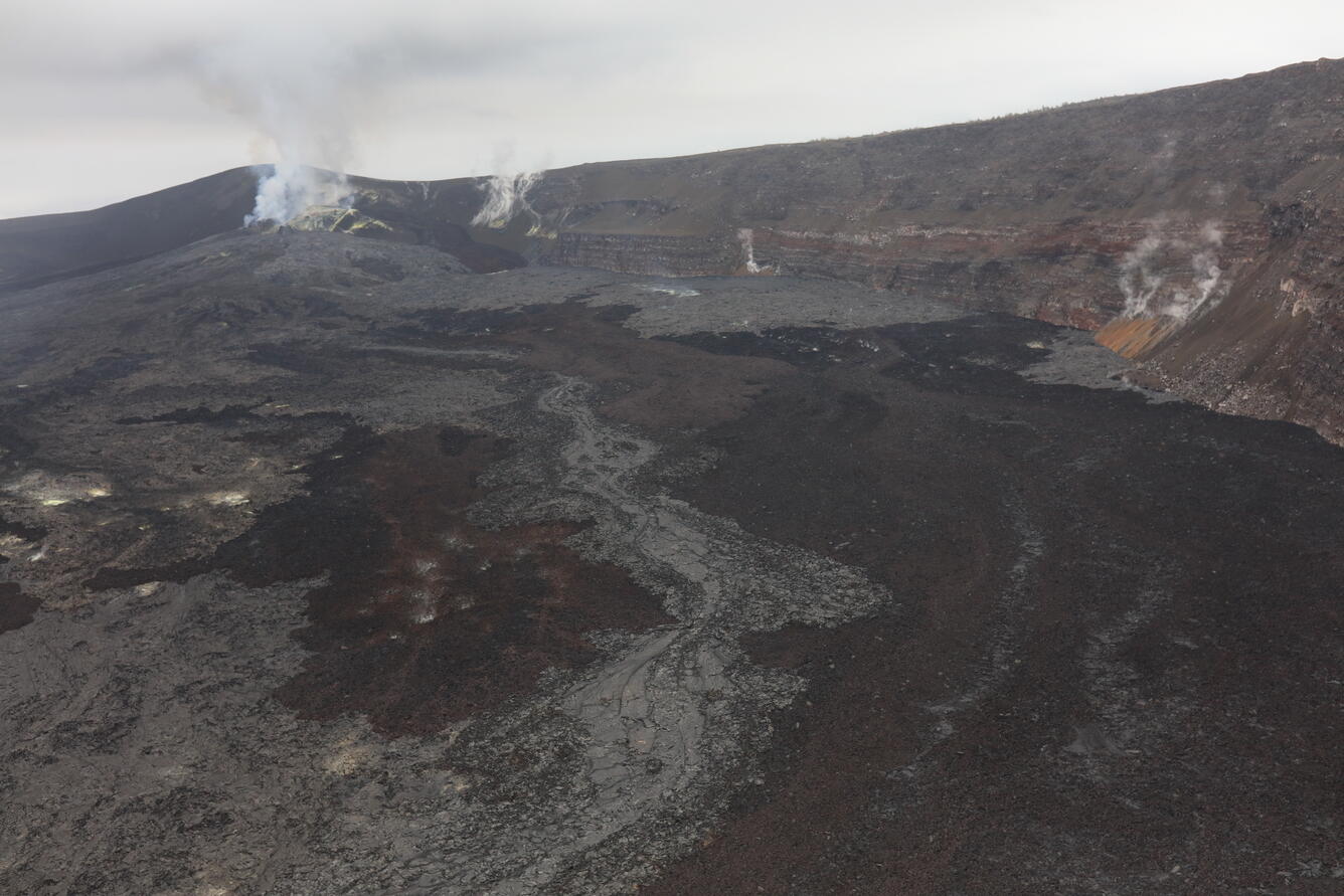 Dark lava flows cover a crater beneath steaming vents.