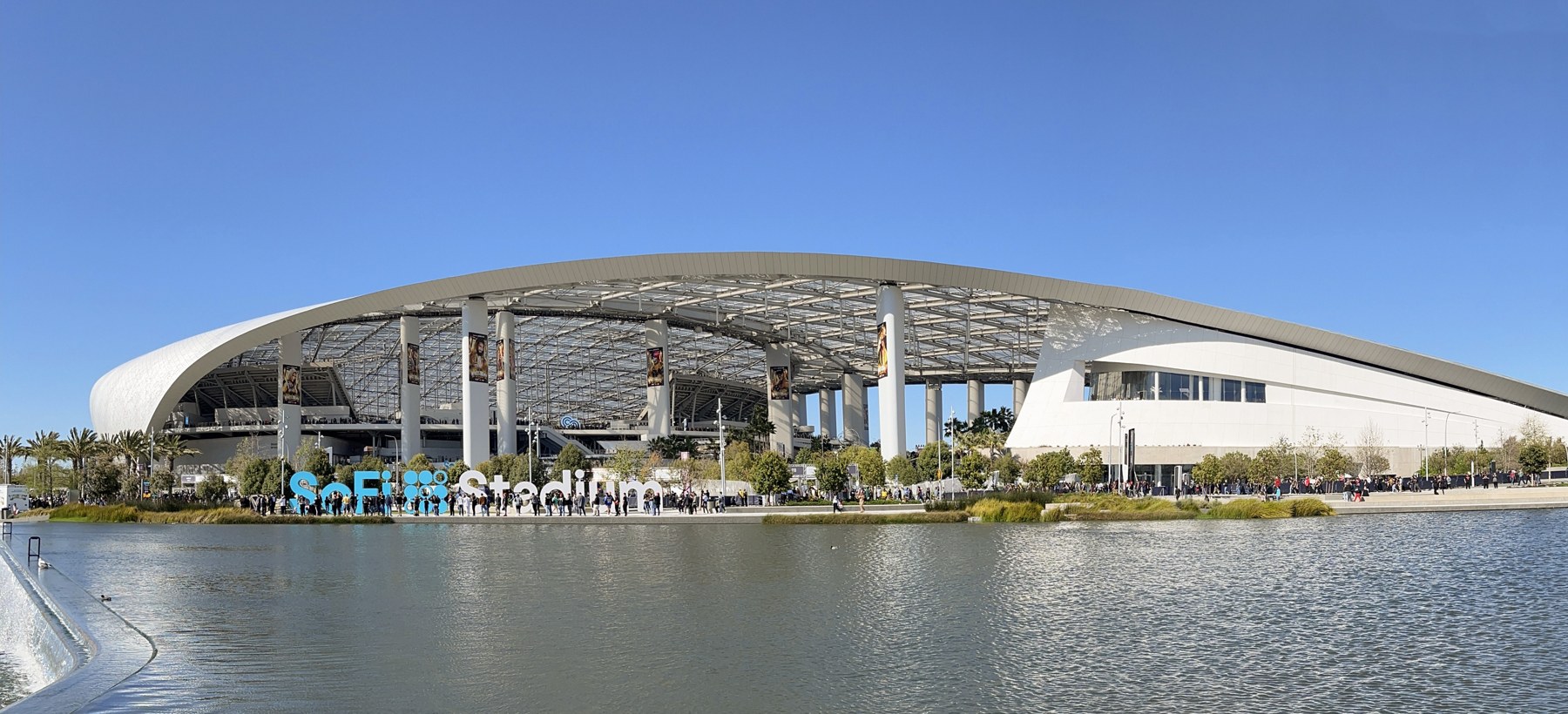 SoFi Stadium’s curved roof and exterior beside a reflecting pool.
