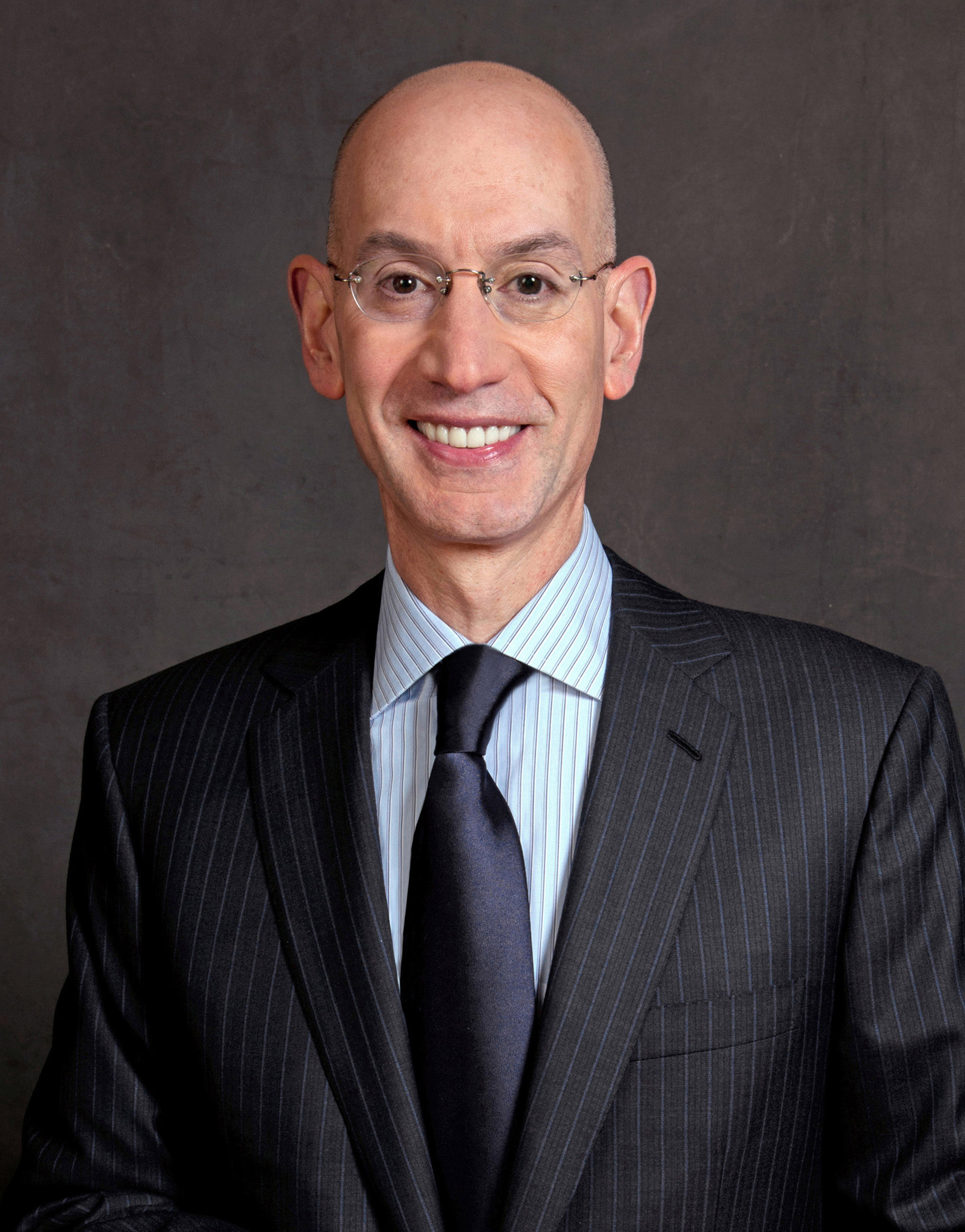 Adam Silver wearing a suit and glasses against a plain background.