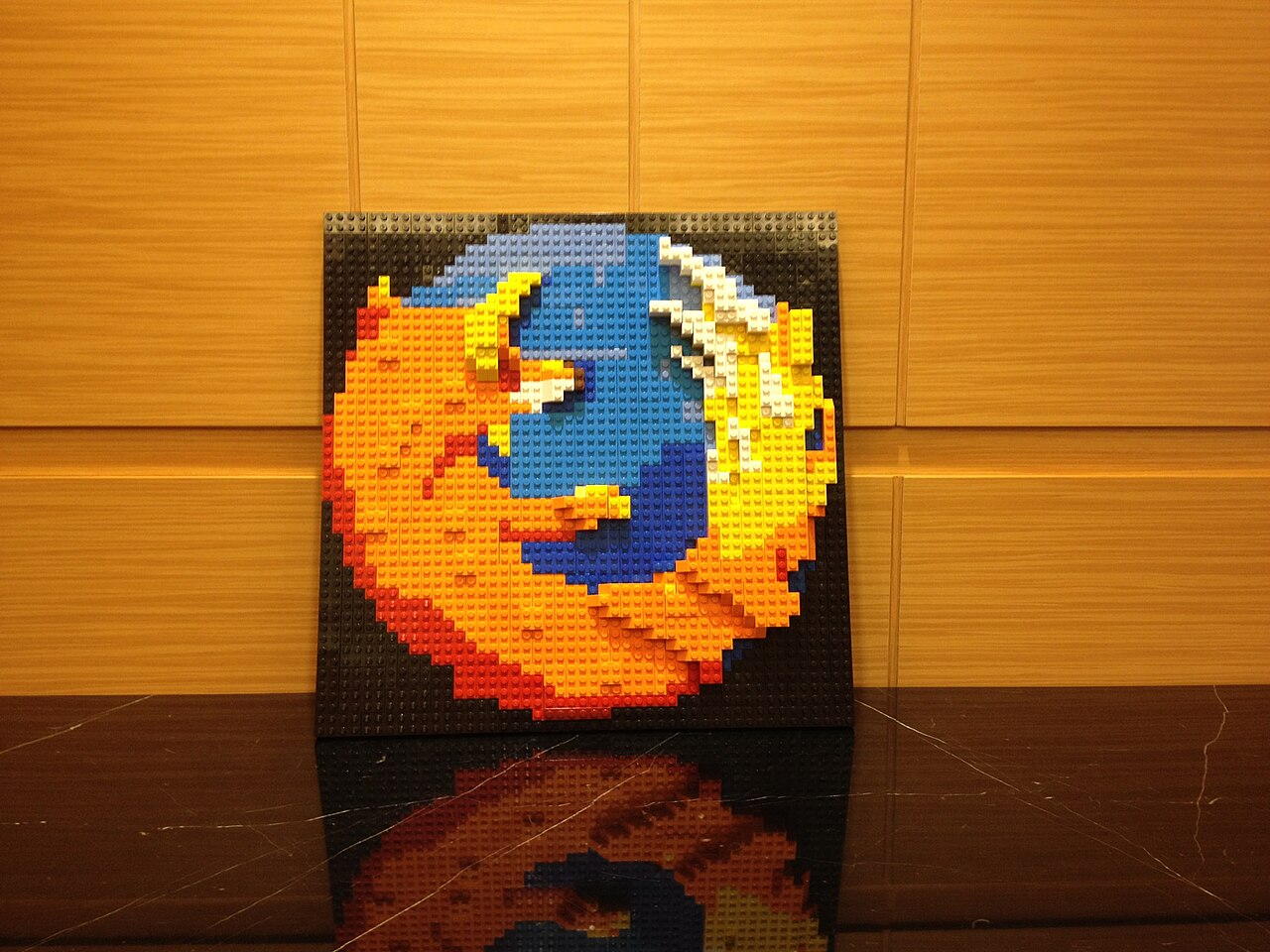 A Firefox logo assembled from bricks against wood paneling.