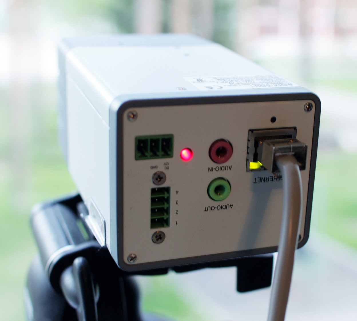 The rear of an IP camera with an Ethernet cable, audio ports and indicator lights.