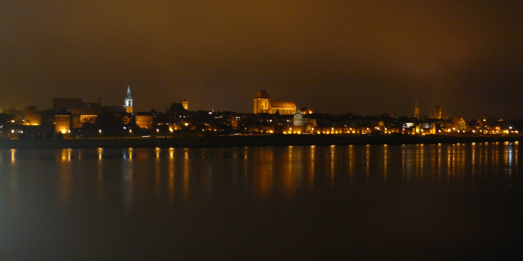 Toruń’s illuminated riverside skyline reflected in the Vistula at night.