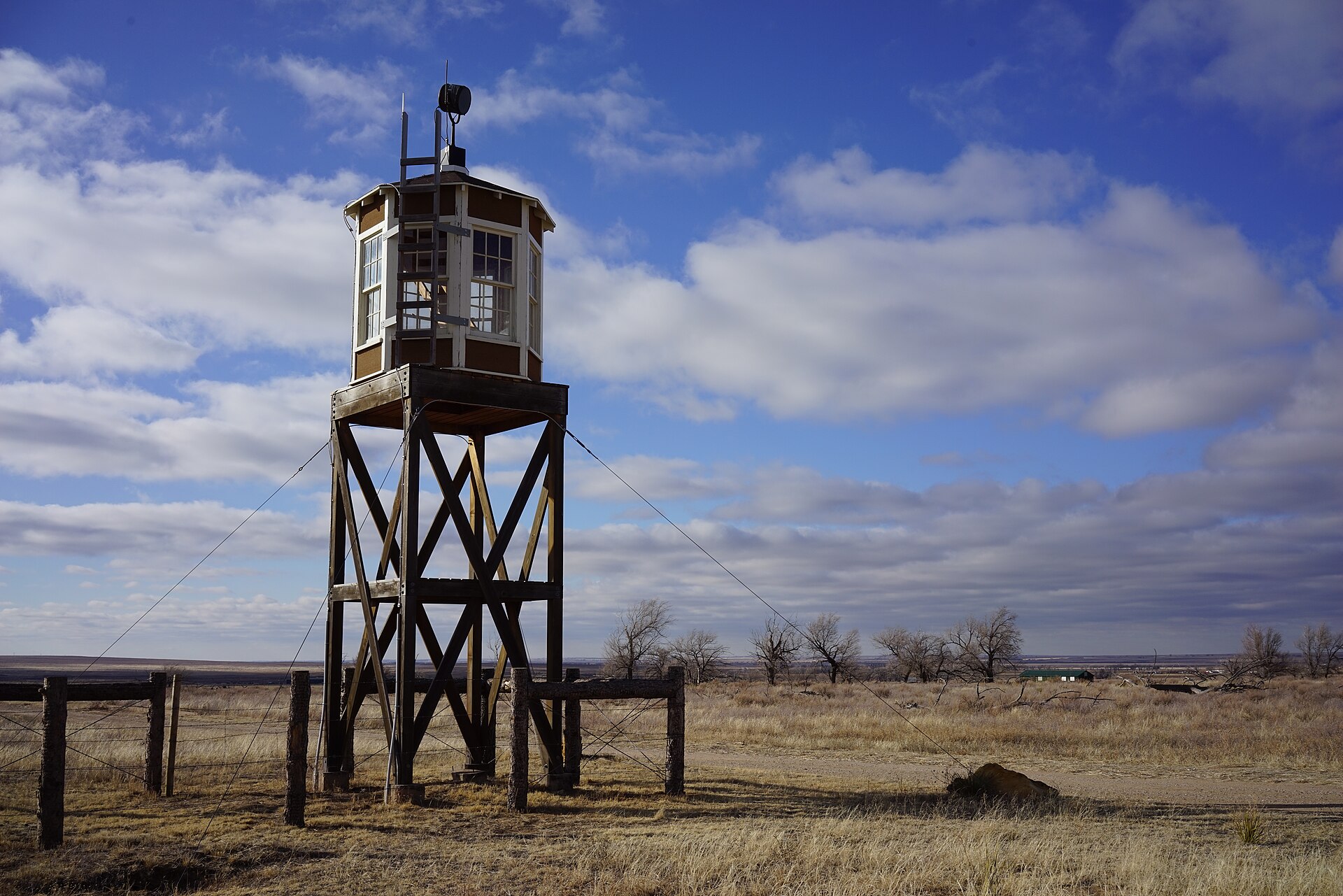 A wooden guard tower above prairie under a cloudy blue sky.