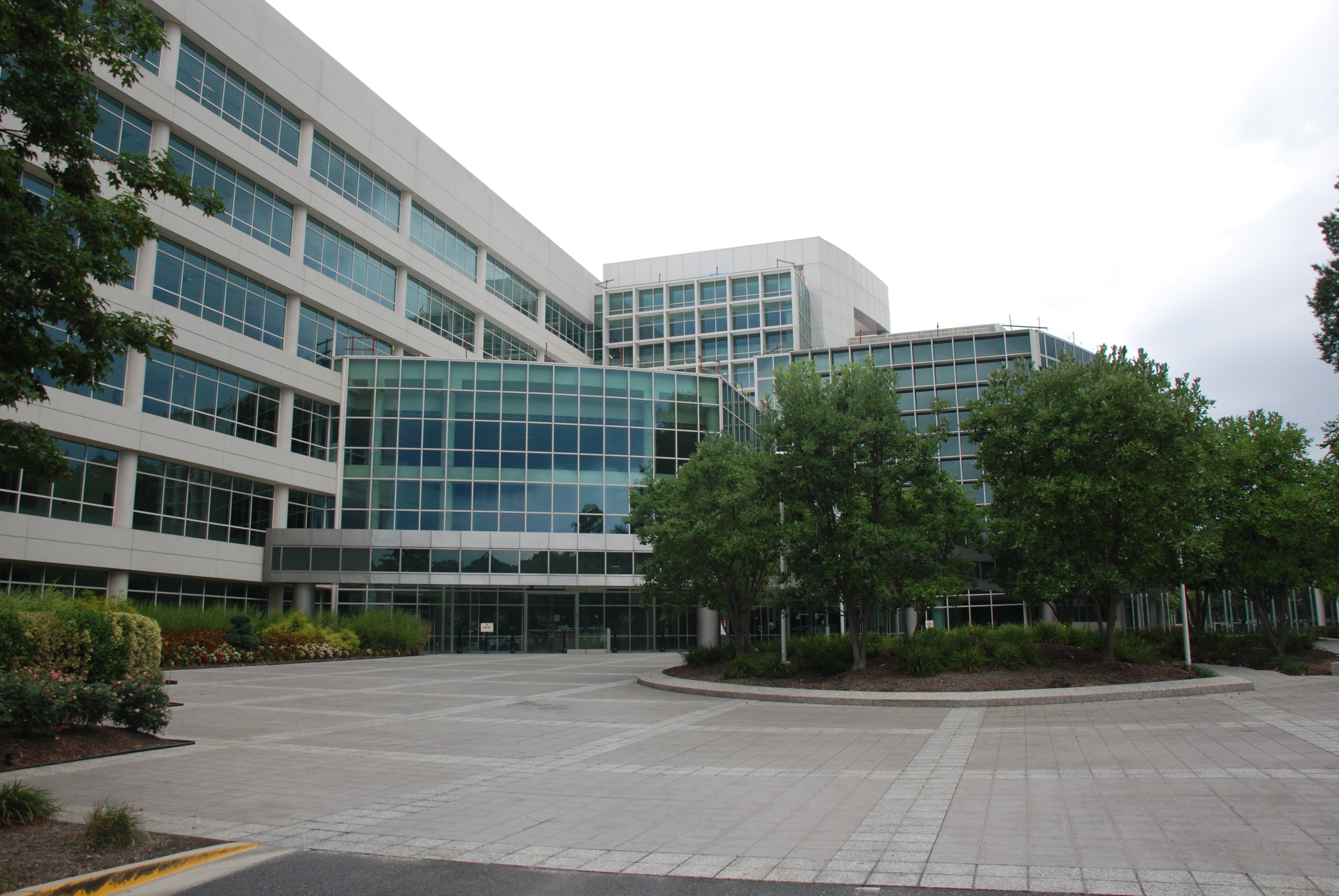 Glass-fronted National Archives buildings around a paved entrance courtyard with trees.
