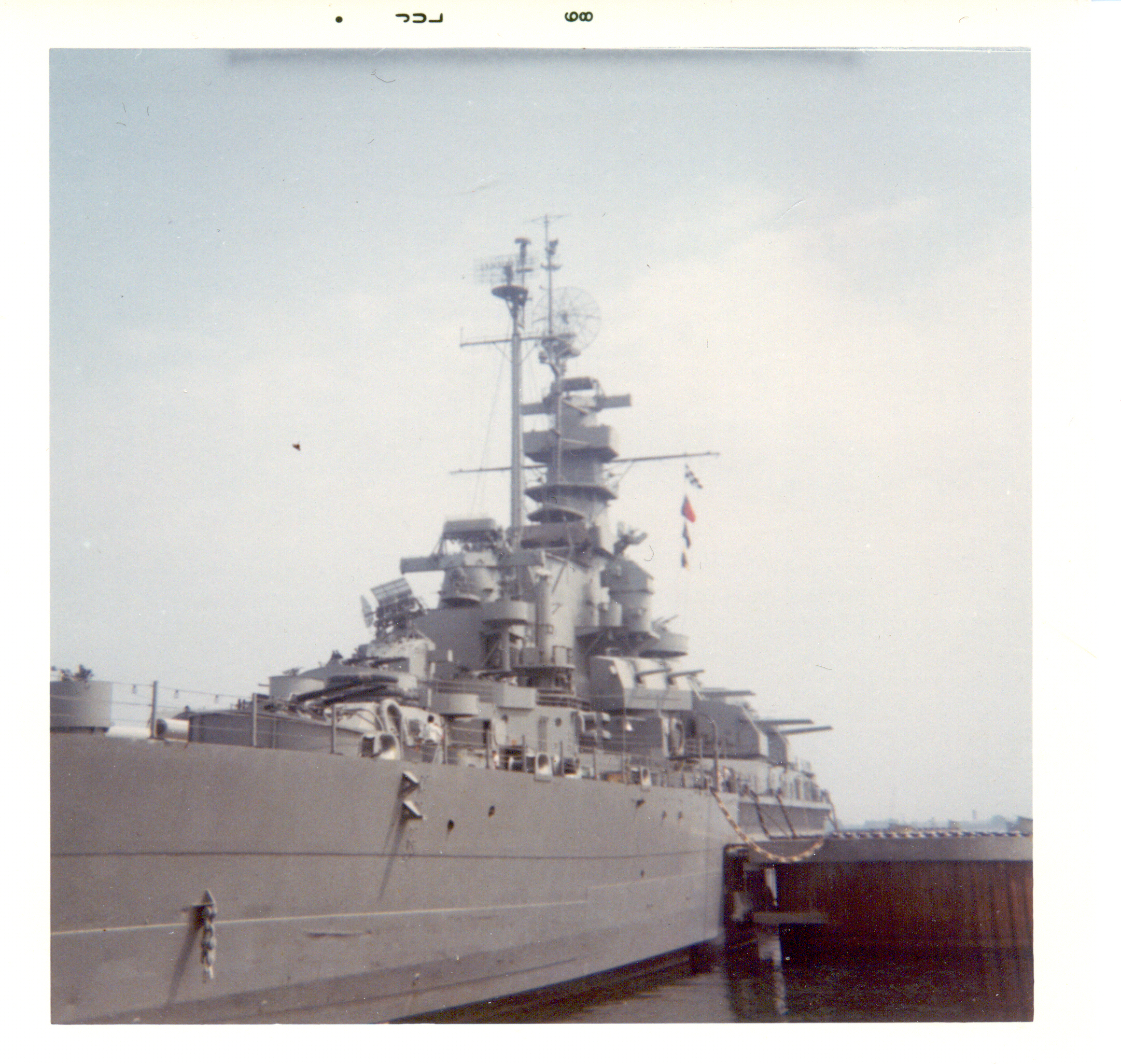 The battleship’s gray port side and superstructure seen from a pier.