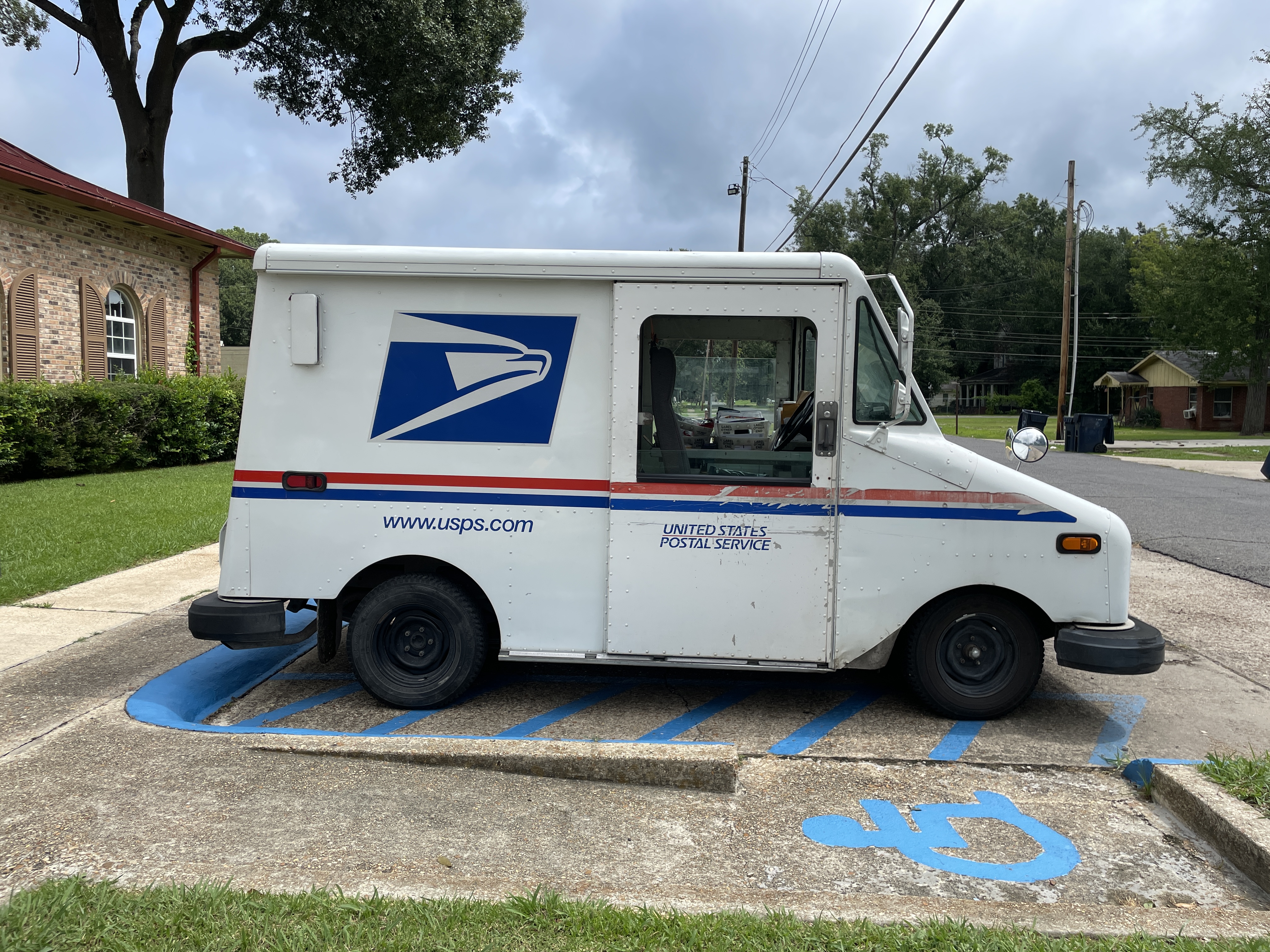 A white USPS delivery truck parked beside a brick building.