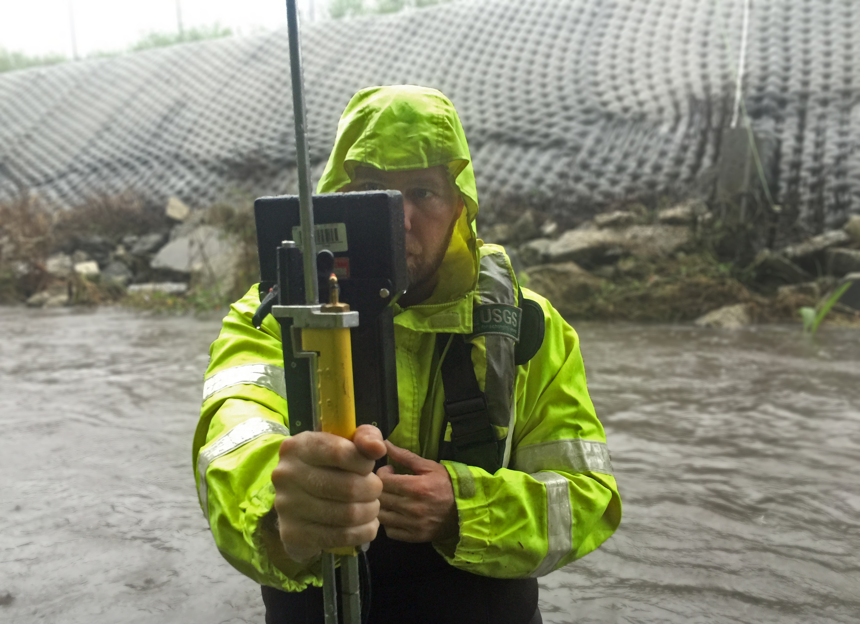 Technician in rainwear holds a streamflow measurement instrument.
