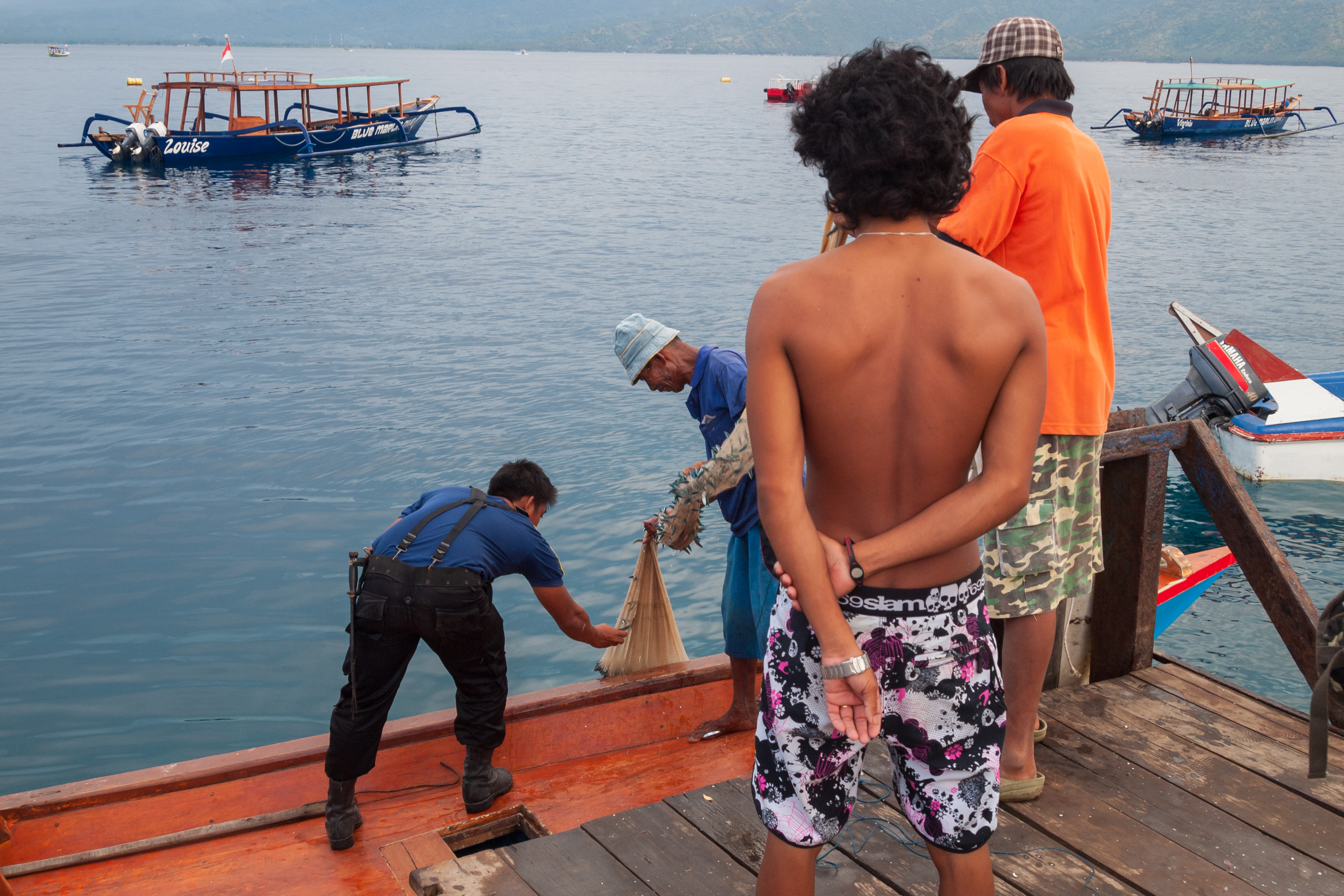 People handle fishing gear beside a small boat.