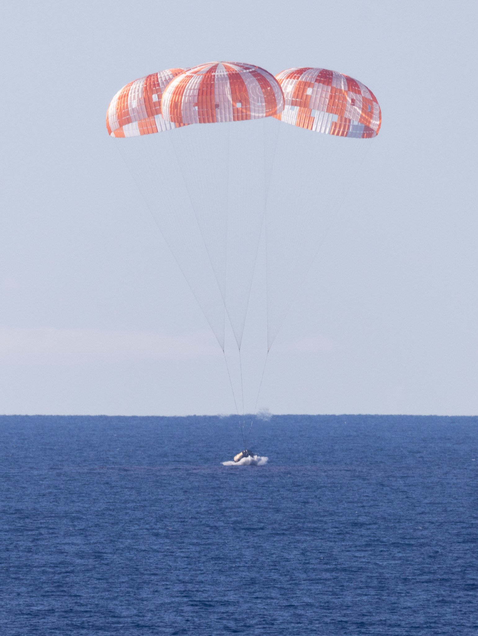 Orion capsule touching the ocean under three parachutes.