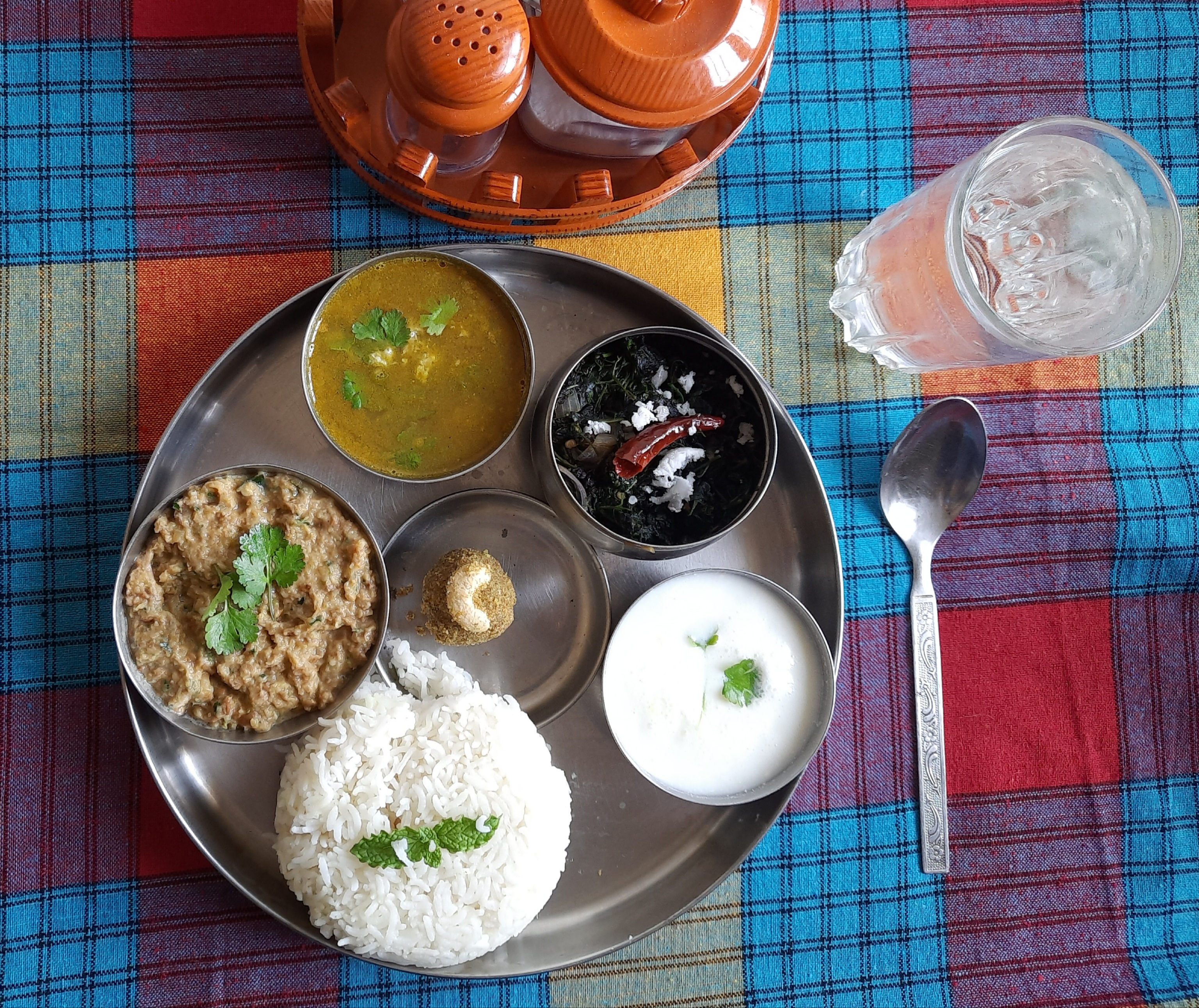 A metal platter with white rice and several small dishes beside a spoon and water glass.