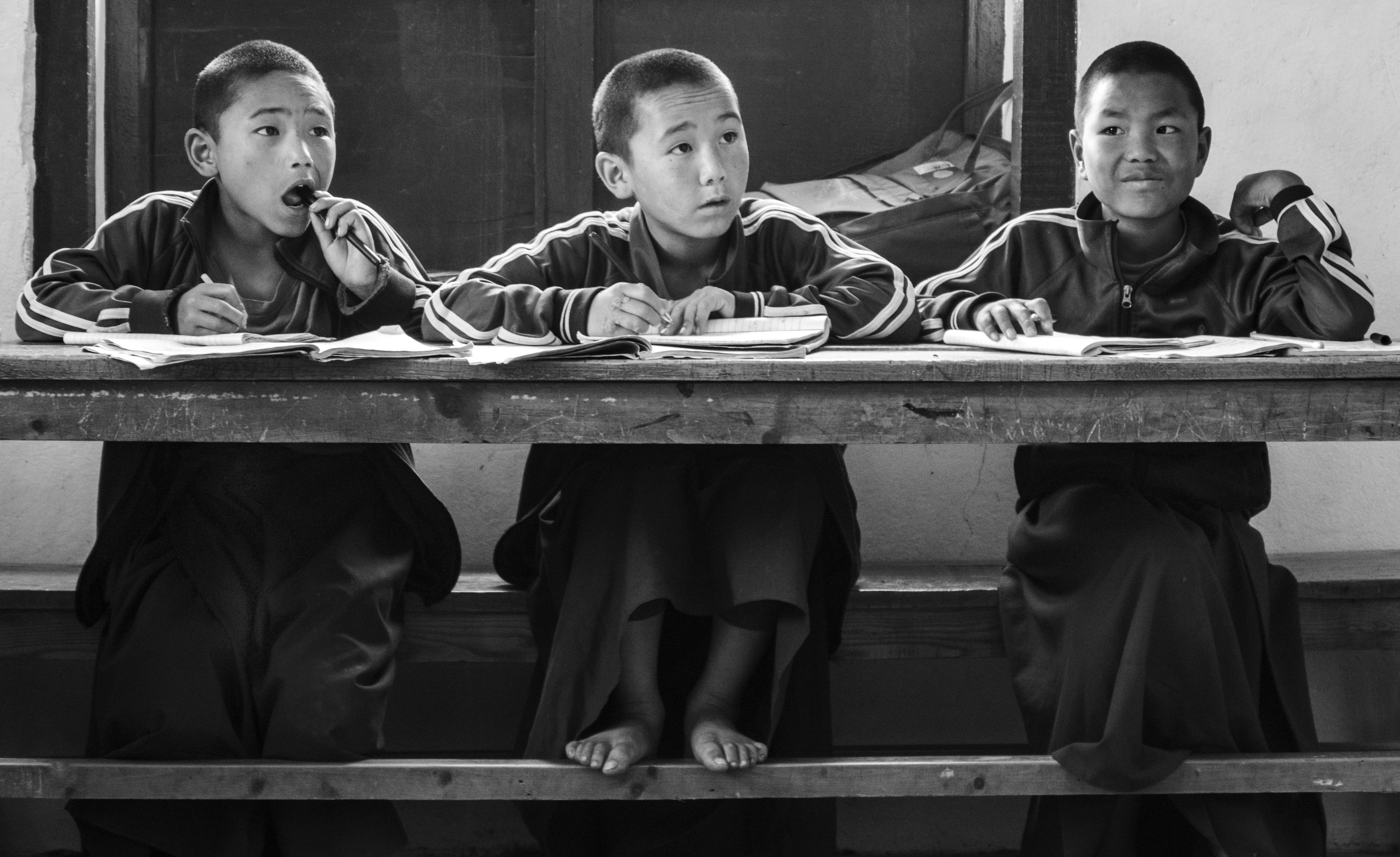 Three pupils seated at a wooden desk with open books in a Nepalese classroom.
